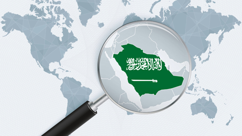 A graphic map of the world in light grey and white with a magnifying glass hovering over the Arabian Peninsula showing the kingdom of Saudi Arabia highlighted with their flag, a green background with Arabic script and the outline of a sword underneath in white