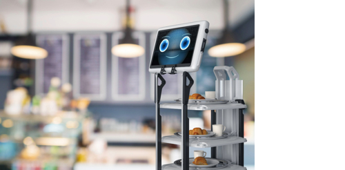 – An image representing the idea of a service robot, featuring a robot with shelves on which plates of food are stored, and a screen with a friendly face. In the background is a blurred image suggesting the interior of a café.